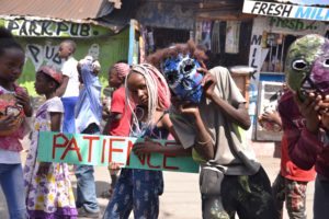 The photo shows African children around 10 years old. The girl in the middle is looking into the camera, she has blond-red dyed rasta braids and holds a sign with the inscription 