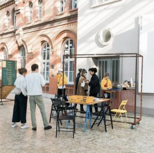 Stellwerk at the Kassel main railway station. The photo shows young people standing in front of the building drinking coffee, discussing. In the middle provisionally placed tables, chairs.