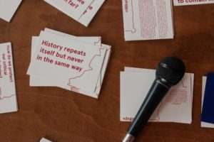 Small stacks of cards on a brown table, with a microphone on top. One of the cards reads 