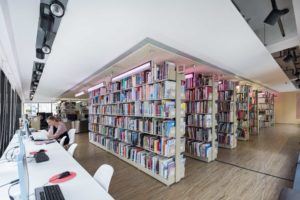 A photo from the Asia Art Archive Library. There are shelves of books in the middle and a visitor is sitting at a computer on the left edge of the picture.