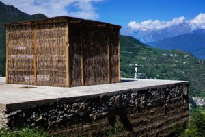 A bamboo hut on a roof of a building. In the background a residential area in a mountainous, green landscape.