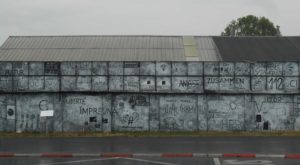 A building, the outer wall is painted with white and black permanent marker. Various terms and paintings can be seen.