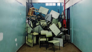 School desks and chairs stacked chaotically at the end of a blue hallway.