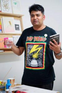 Hamja Ahsan mit einem Glas und Buch in der Hand.