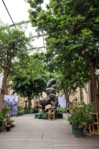 Installation view. In the center of the picture is a sculpture, it is surrounded by trees and information boards.