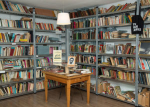 A section of a room from The Black Archives. There is a small table in the middle and shelves filled with books on the walls.