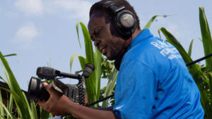 A man stands in front of green plants and films something with a camera