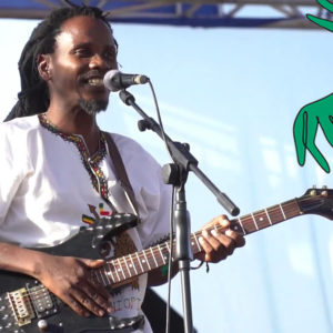 Ein afrikanischer Musiker mit E-Gitarre singt ins Mikrofon.