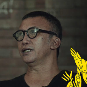 An Indonesian man with glasses, short hair looks into the distance while he speaks.