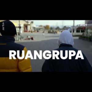 Photo shows two people from behind with hood and cap. They are walking towards the city center of Kassel. White writing underneath ruangrupa.