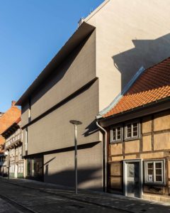 Fotografie eines modernen Gebäudes zwischen zwei kleinen Fachwerkhäusern.