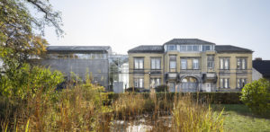 Das Foto zeigt das Gebäude des Museums für Sepulkralkultur sowie die Grünfläche davor, die aus einem kleinen Teich, Gräsern und Sträuchern besteht.
