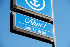 The photo is a close-up of a sign outdoors, with a bright blue sky behind it. The sign is blue and with white lettering it says in German language: 