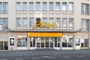 The photo shows the building facade of the cinema in simple 50s style. Above the entrance glass doors, the name of the cinema 