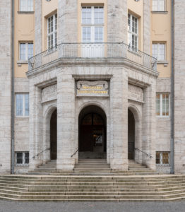 The photo shows the facade of the entrance area of Hessisches Landesmuseum. Above the middle of the three stone door arches is written in golden color: 