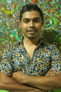Portrait photo of Putra Hidayatullah in a colorful shirt in front of a colorful wall.
