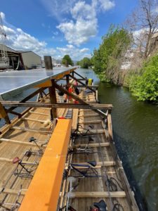 Photo from above on the wooden ship without roof. Bicycle racks and some people in front. In the background the city, good weather, some green.