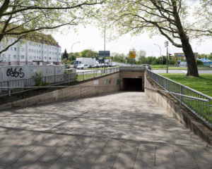 Auf dem Foto sieht man den Eingang der Fußgänger*innenunterführung am Platz der deutschen Einheit. Im Hintergrund sind Autos zu sehen.