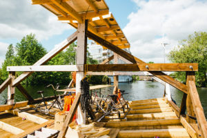 Aus einem Holzdach gebaute Floßähnliche Schiff auf dem Fluss. Darauf Fahrradgestelle.